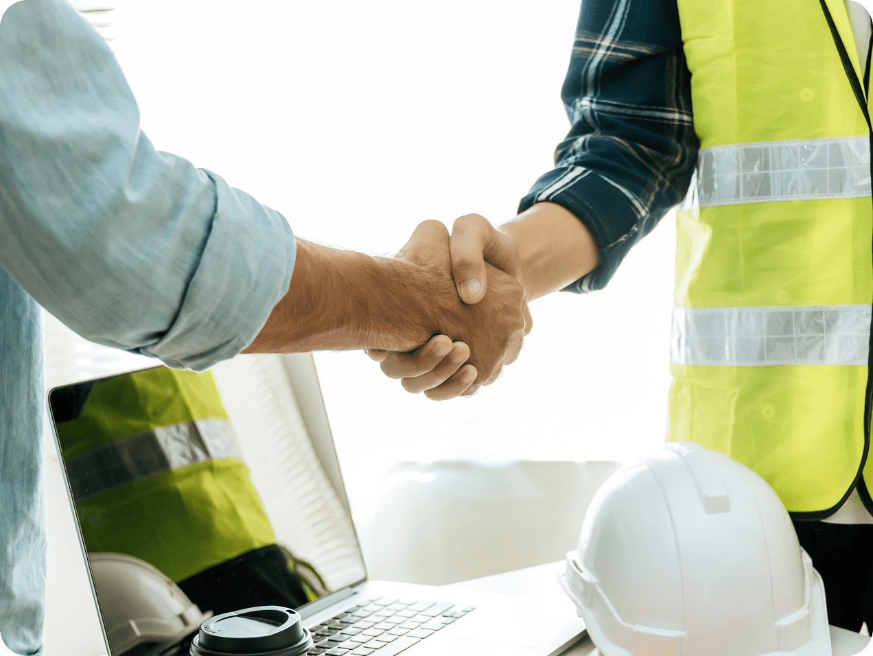 Handshake between engineer and colleague near laptop.